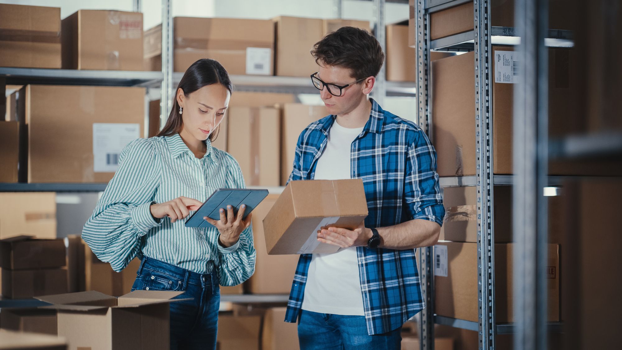 one female and one male, are Two employees entering inventory data into the computer system to reflect an available product stored in a warehouse