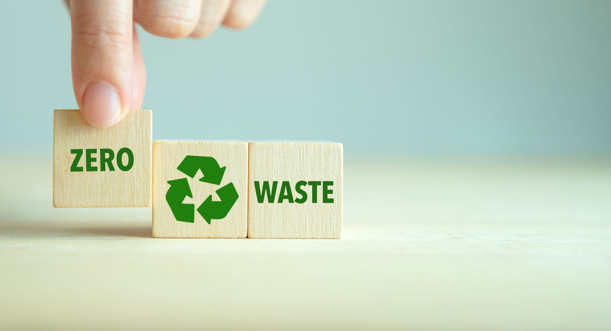 A hand placing the wooden block with "zero" word in front of recycle icon