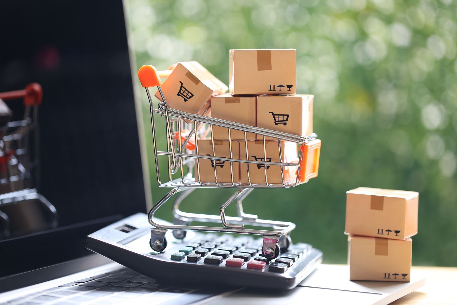 Miniature cart and shipping boxes placed on top of a laptop and calculator