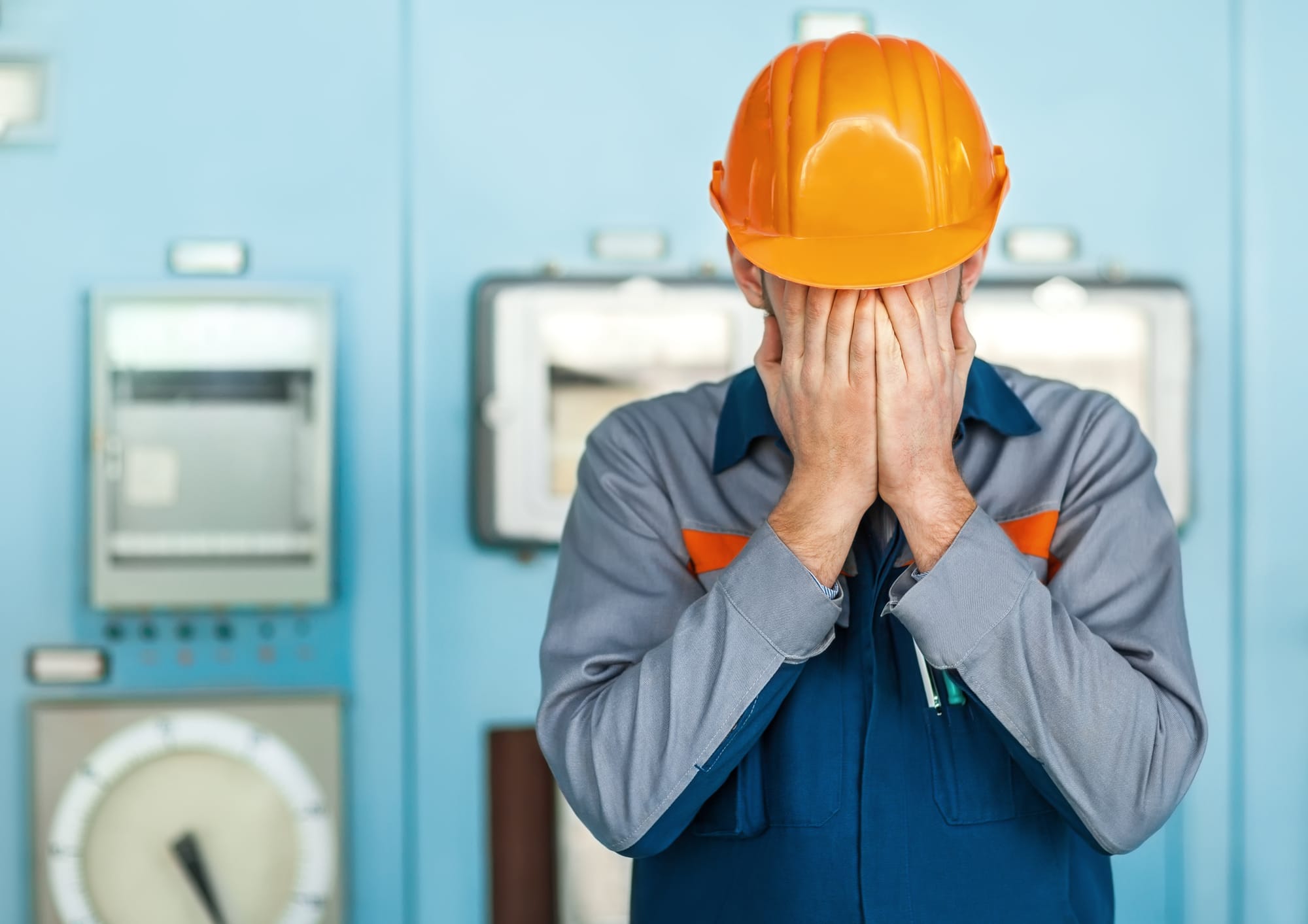 A man wearing a yellow safety hat covering his face with two hands.