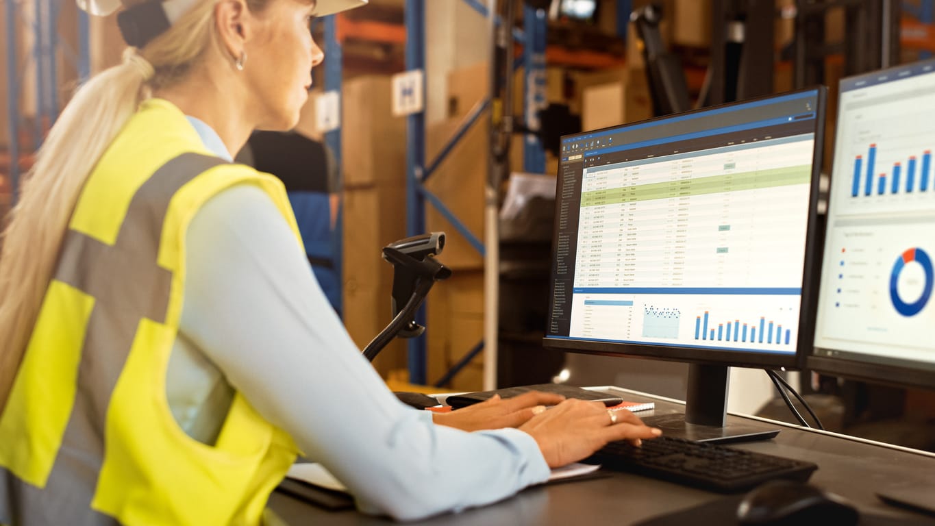 A woman in a warehouse managing inventory records on her computer.