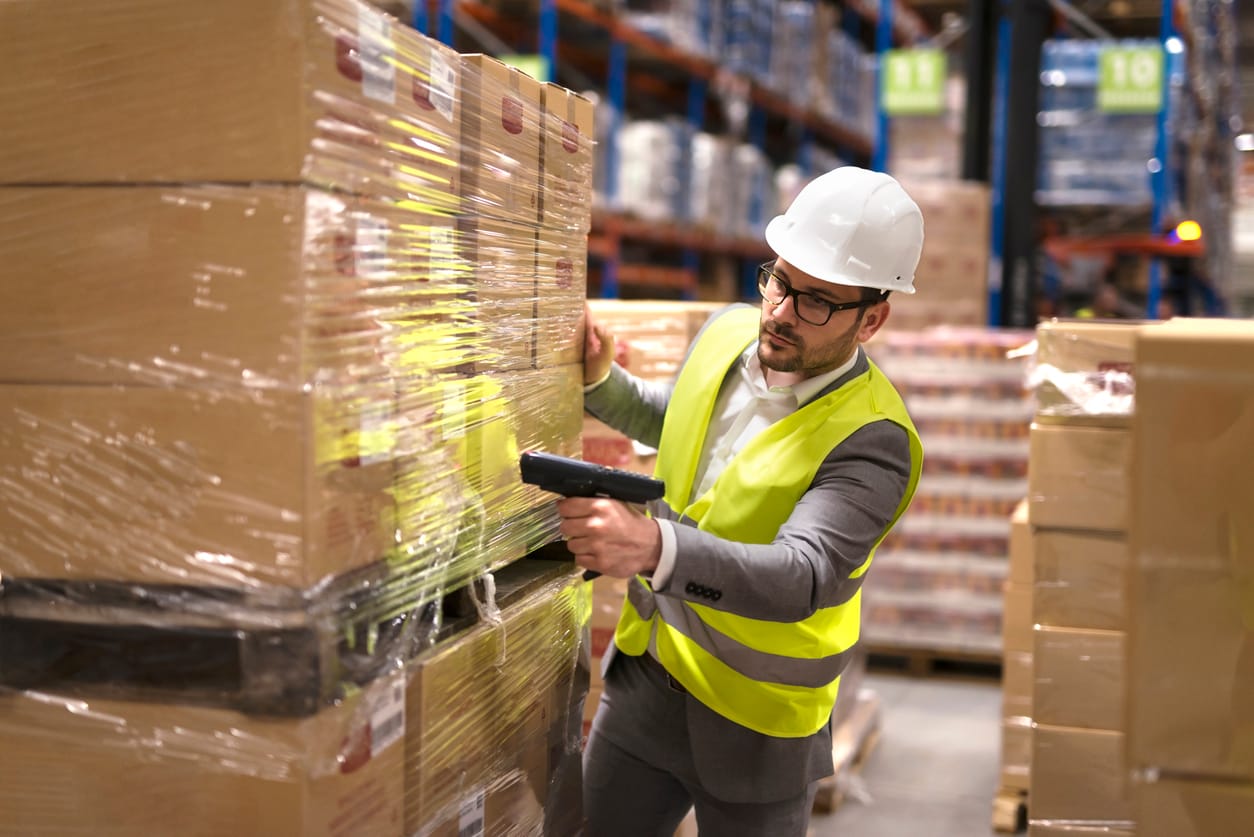 Male warehouse staff with a helmet scanning large boxes