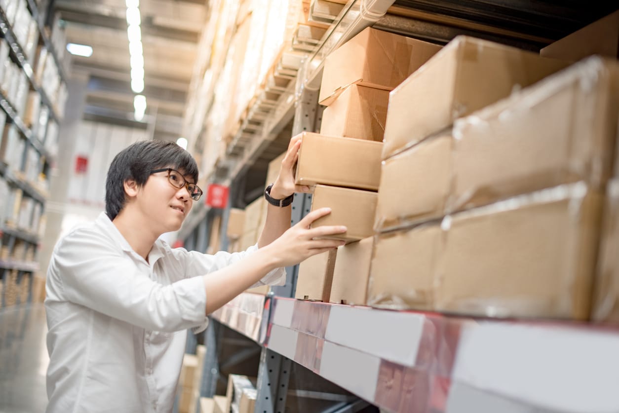 Asian man organizing boxes of inventory on warehouse shelves