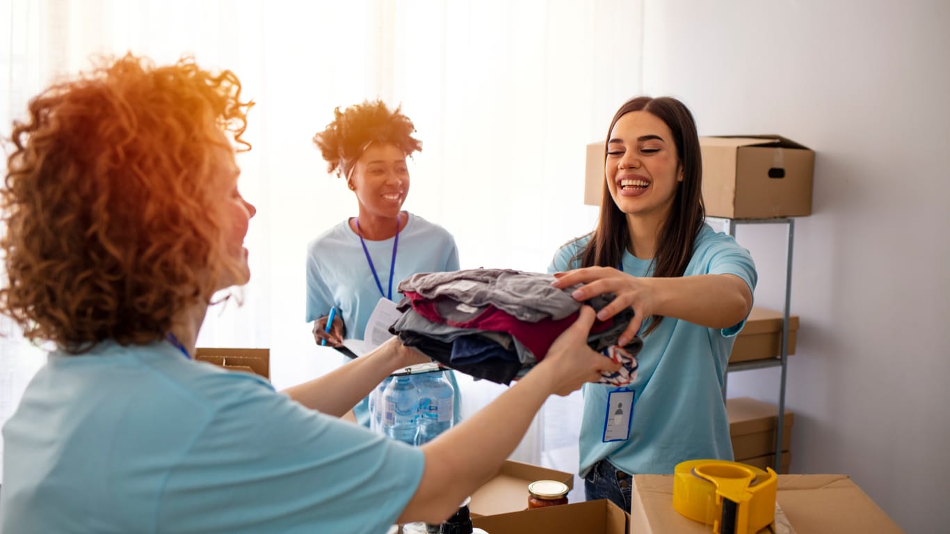 Happy team of volunteers holding donations boxes in a large warehouse