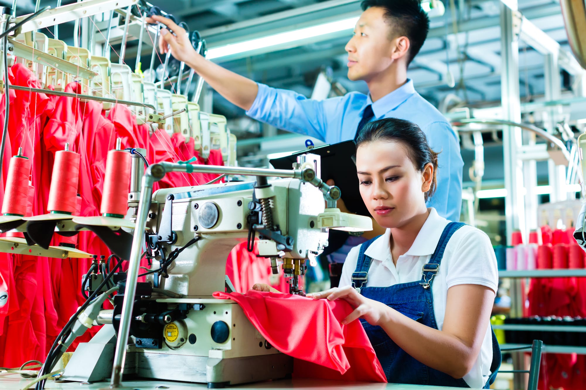 A female worker in a factory with a sewing machine, a foreman checks the yarn