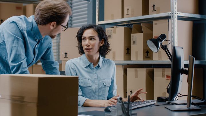 A male and a female employees having conversation by checking inventory level at the desk in a warehouse