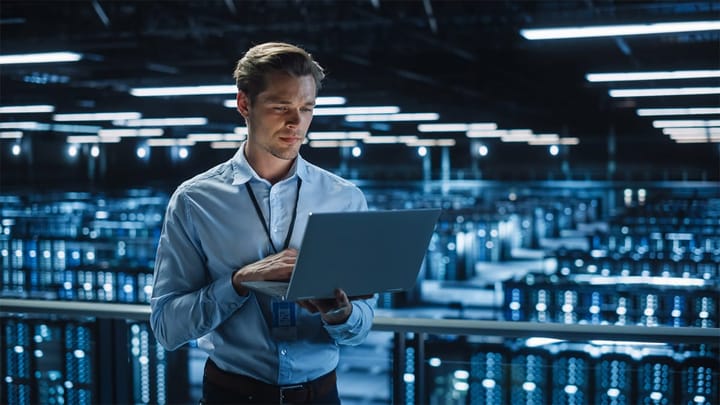 Handsome Smiling IT Specialist Using Laptop Computer in Data Center.