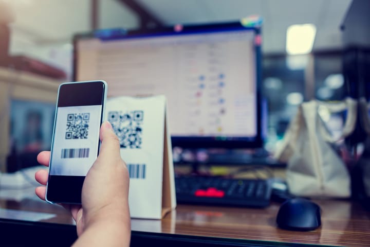 A person holding a smartphone to scan a QR code with blurry computer screen in the background